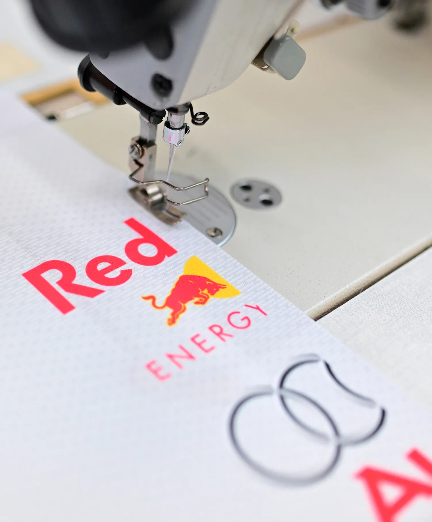 Una macchina da cucire sta cucendo un capo sportivo bianco con il logo Red Bull Energy.